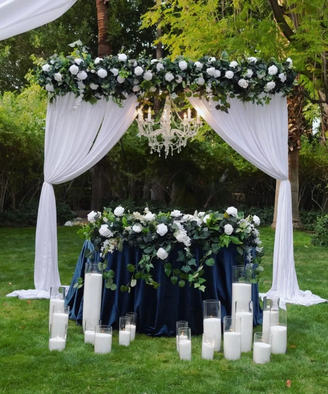 Masă de ceremonie în aer liber, cu față de masă bleumarin, trandafiri albi, candelabru de cristal și lumânări în sticlă