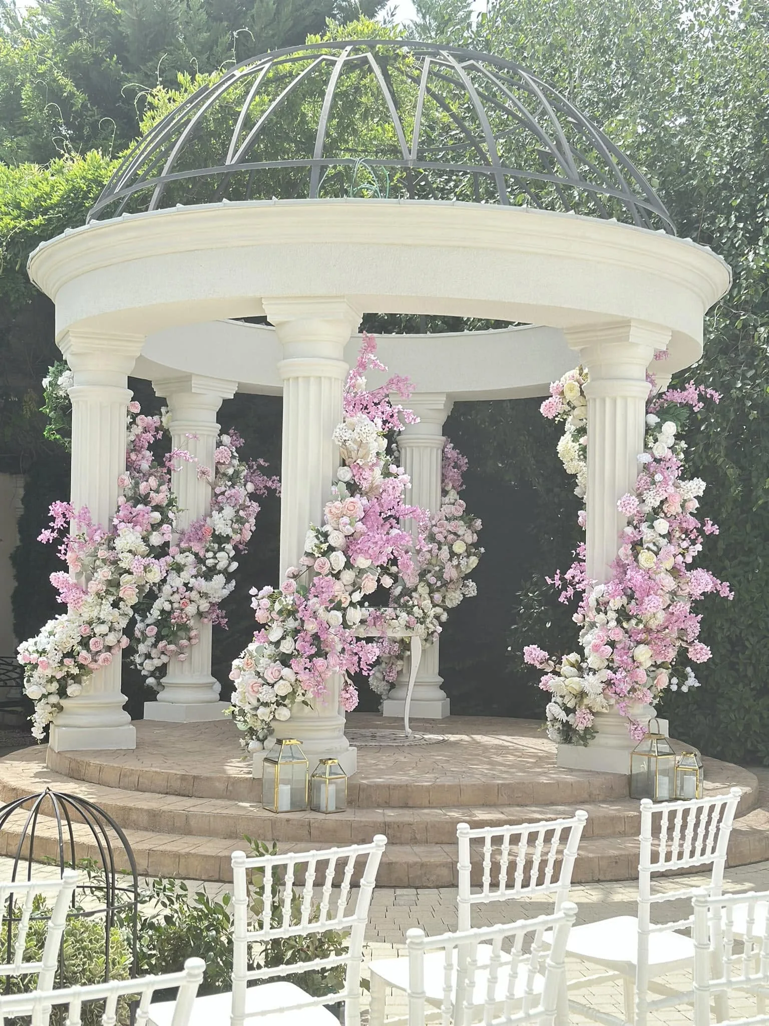 Gazebo alb cu coloane, îmbrăcat în compoziții florale roz și albe, pregătit pentru o ceremonie în aer liber